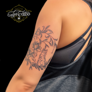 Tatouage haut du bras, au dessus du coude, femme. Réalisation d’une lune florale, végétale, en fleurs et feuillages, avec une silhouette de chat de dos. Réalisation dans le,meilleur salon de tatouage de Gironde à Villenave d’Ornon à côté de Blanquefort et Saint André de Cubzac.