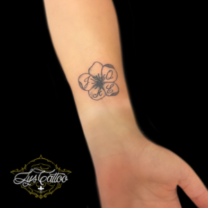 Tatouage poignet femme, fleur minimaliste et initiales. Réalisation par les meilleurs tatoueurs de Bordeaux à Gradignan proche de Gujan Mestras et Bruges en Gironde.