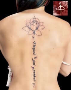 Tatouage de fleur de lotus sur la colonne vertébrale avec l'inscription "Perfect, just perfect", réalisé par Lys Tattoo.