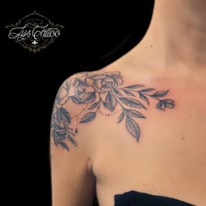 Tatouage floral délicat avec roses et feuillage couvrant l'épaule et la clavicule, réalisé par Lys Tattoo.