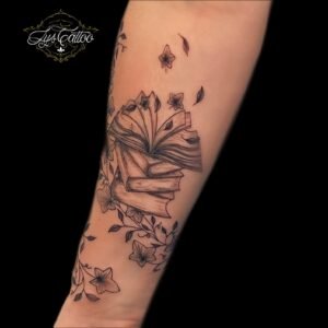 Tatouage de livres ouverts avec motifs floraux et feuilles grimpantes, réalisé par Lys Tattoo.