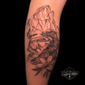 Tatouage de lion avec montagnes, fleurs et papillon sur l'avant-bras, réalisé par Lys Tattoo.