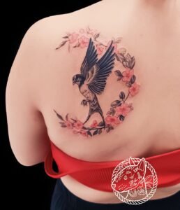 Tatouage d'oiseau en vol entouré de fleurs roses sur le dos, réalisé par Le Bull Tatoué.