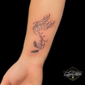 Tatouage fin et élégant représentant un phénix stylisé au poignet, avec des courbes délicates et des feuilles intégrées au design, symbolisant la renaissance et la transformation.