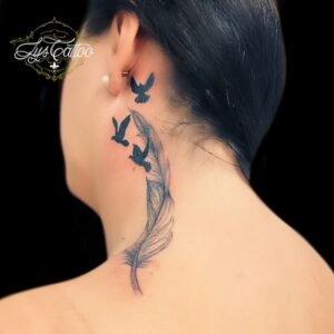 Tatouage délicat derrière l’oreille représentant une plume fine se transformant en trois oiseaux en vol, symbole de liberté, espoir et légèreté.