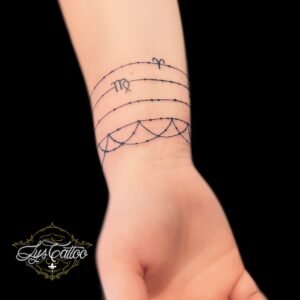 Tatouage bracelet fin avec signes astrologiques en calligraphie et ornements en perles sur le poignet, réalisé par Lys Tattoo à Villenave d’Ornon, proche de Bordeaux, Pessac et Talence.