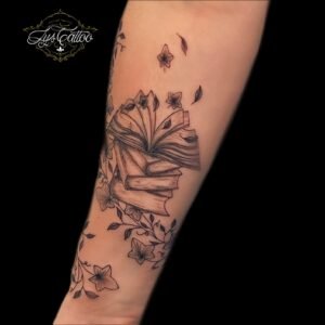 Tatouage artistique de livres ouverts entourés de fleurs et de feuilles, réalisé par Lys Tattoo au salon Lys Tattoo à Gradignan, près de Bordeaux.