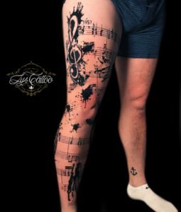 Tatouage manchette musicale avec notes, clé de sol et éclaboussures d’encre en noir sur la jambe, réalisé par Lys Tattoo chez Lys Tattoo à Gradignan (Bordeaux)