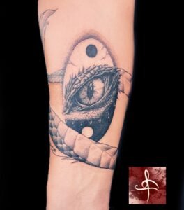 Tatouage d'œil de reptile réaliste entouré d'un symbole yin-yang, avec des détails minutieux de texture et d'ombre, réalisé par Rhum1 Tattoo au Lys Tattoo.