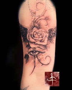 Tatouage monochrome représentant une rose aux ailes d'ange, avec un œil d'Horus et des motifs floraux ornés, réalisé par Rhum1 Tattoo au salon Lys Tattoo.