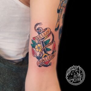 Tatouage rétro nautique représentant une ancre ornée de fleurs et de rubans portant l'inscription "Hello Sailor", réalisé par Le Bull Tatoué au salon Lys Tattoo.