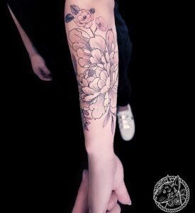 Tatouage floral noir et gris avec grandes fleurs détaillées et feuillages, réalisé sur l’avant-bras par Le Bull Tatoué au salon Lys Tattoo.