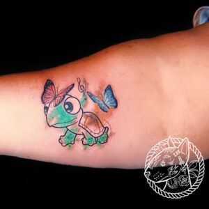 Tatouage coloré de petite tortue avec des papillons sur l’avant-bras, réalisé par Le Bull Tatoué au salon Lys Tattoo.