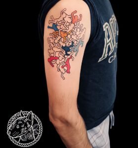 Tatouage artistique de personnages entremêlés et colorés sur le haut du bras, réalisé par Le Bull Tatoué au salon Lys Tattoo.