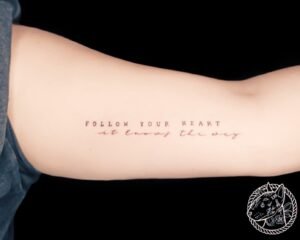Tatouage minimaliste avec citation "Follow your heart, it knows the way" sur le bras, réalisé par Le Bull Tatoué au salon Lys Tattoo.