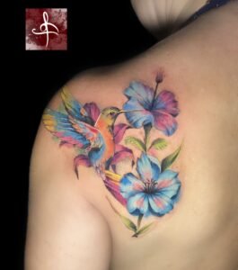 Tatouage colibri en couleurs vives avec fleurs bleues, style aquarelle réaliste – Rhum1 Tattoo Bordeaux