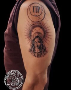 Tatouage Vierge stylisée en noir et gris, halo rayonnant et symbole astrologique – bras