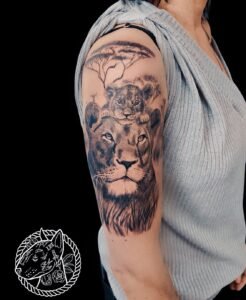 Tatouage lionne et lionceau réalisme noir et gris, savane et acacia, haut du bras