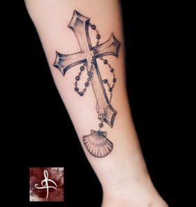 Tatouage croix en dotwork avec chapelet et coquille Saint-Jacques sur l’avant-bras, noir et gris, Rhum1 Tattoo.