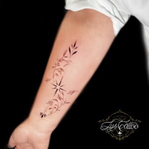 Tatouage ornemental minimaliste avec initiales, feuilles et étoiles sur l’avant-bras