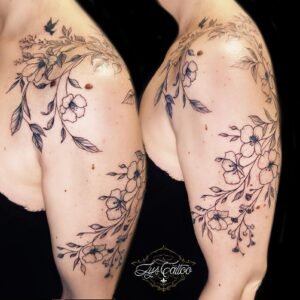 Tatouage floral fin sur l’épaule et le haut du bras, guirlande de fleurs et feuilles