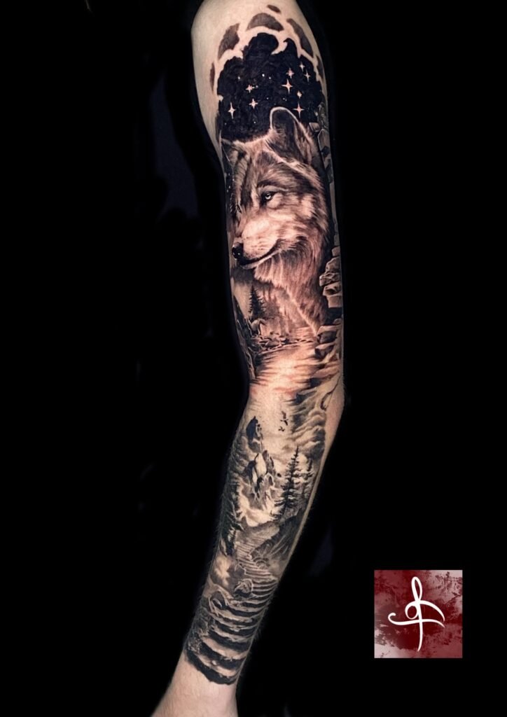 Tatouage manchette réaliste représentant un loup dans un paysage de montagne sous un ciel étoilé, réalisé chez Lys Tattoo à Villenave-d’Ornon près de Bordeaux.